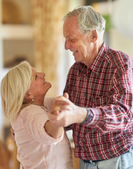 Older adult couple dancing in their home while looking lovingly at each other