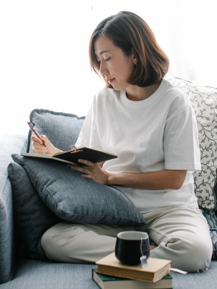 Mid-age woman sitting cross-legged on a sofa and writing in a journal