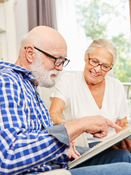Older adult male and female smiling as they look at a photo album together