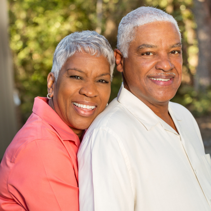 Smiling older adult African American couple standing in front of background of trees