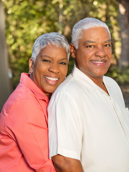 Smiling older adult African American couple standing in front of background of trees