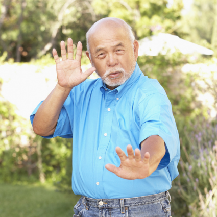 older adult male standing in a Tai Chi pose on grass in a residential backyard