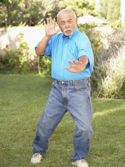 older adult male standing in a Tai Chi pose on grass in a residential backyard 