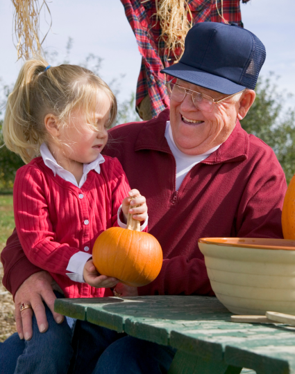 Grandfather and grandaughter laughing while at a picnic table at a pumpkin patch