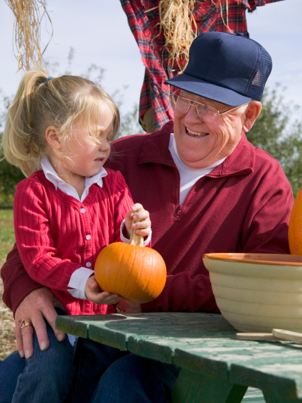 Grandfather and grandaughter laughing while at a picnic table at a pumpkin patch