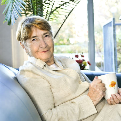 Smiling older adult woman reclining in a chair and holding a cup of coffee