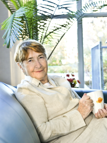 Smiling older adult woman reclining in a chair and holding a cup of coffee