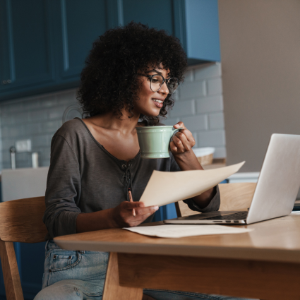 Woman holding a mug and sitting at a table in front of her laptop